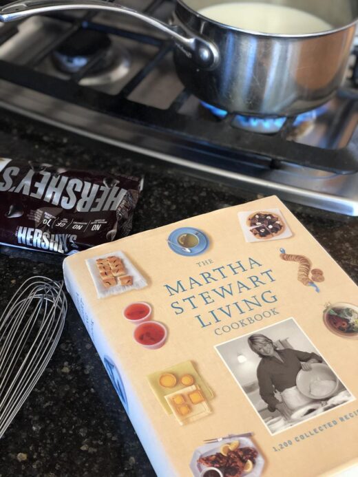 Cooking Martha Stewart's Hot Chocolate in pan with whisk and chocolate next to cookbook