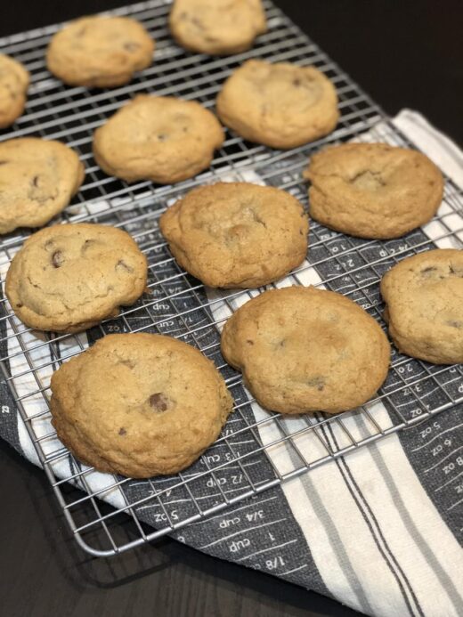 Chocolate Chip Cookies on a cooling rack next to a black and white kitchen towel