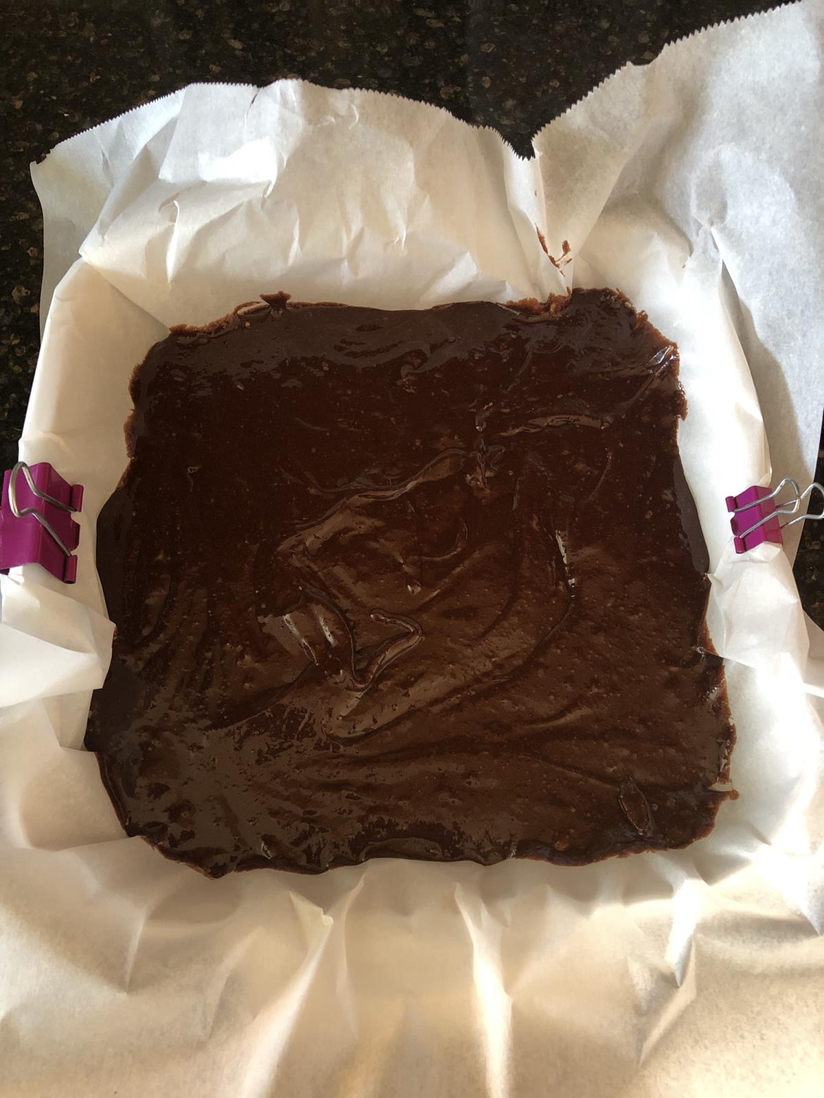 flourless brownie batter in pan with clips holding parchment paper in place