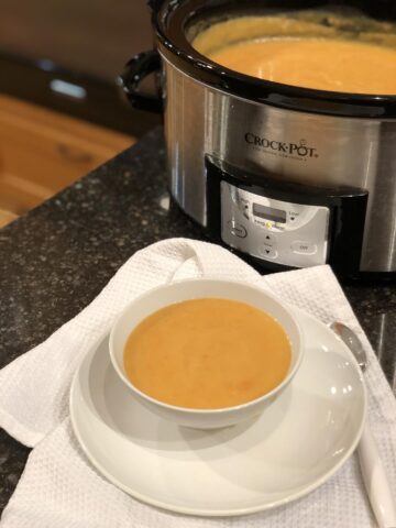 carrot soup in white bowl with crock pot in background