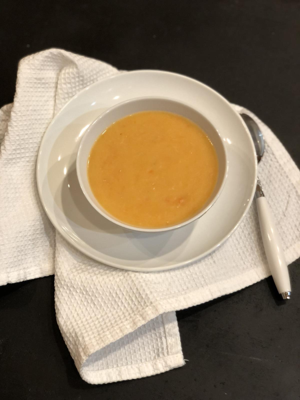 carrot soup in a white bowl on a white towel on a black counter