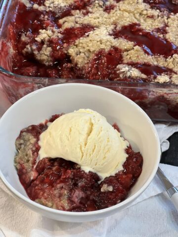 Blackberry cobbler in white bowl with vanilla ice cream