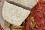 Chicken Salad Sandwich on a white and red plate with chips and tomatoes