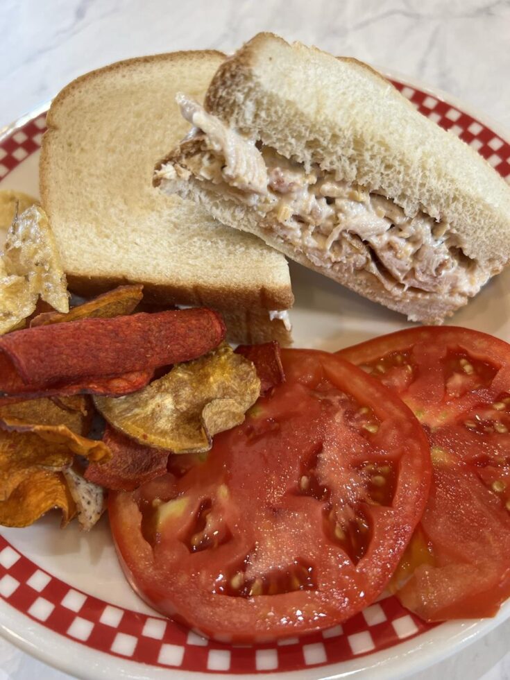 Chicken salad sandwich on a plate with tomatoes and potato chips