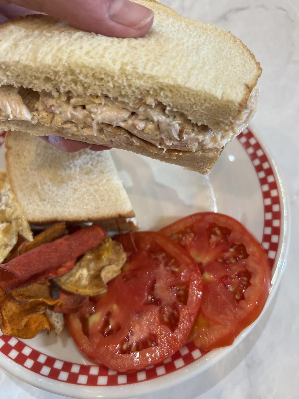 Chicken Salad sandwich with tomatoes and chips on a plate in the background