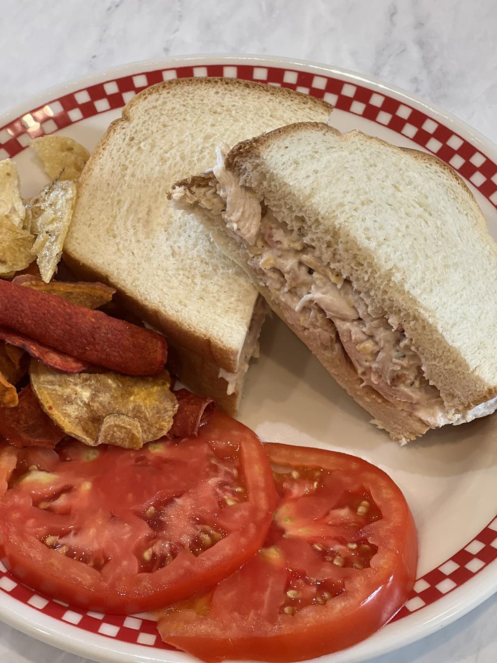 Tomatoes on a plate with a chicken salad sandwich and chips