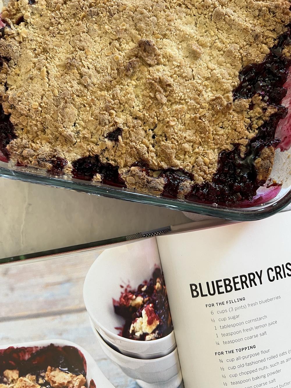 Cookbook with blueberry crisp in background