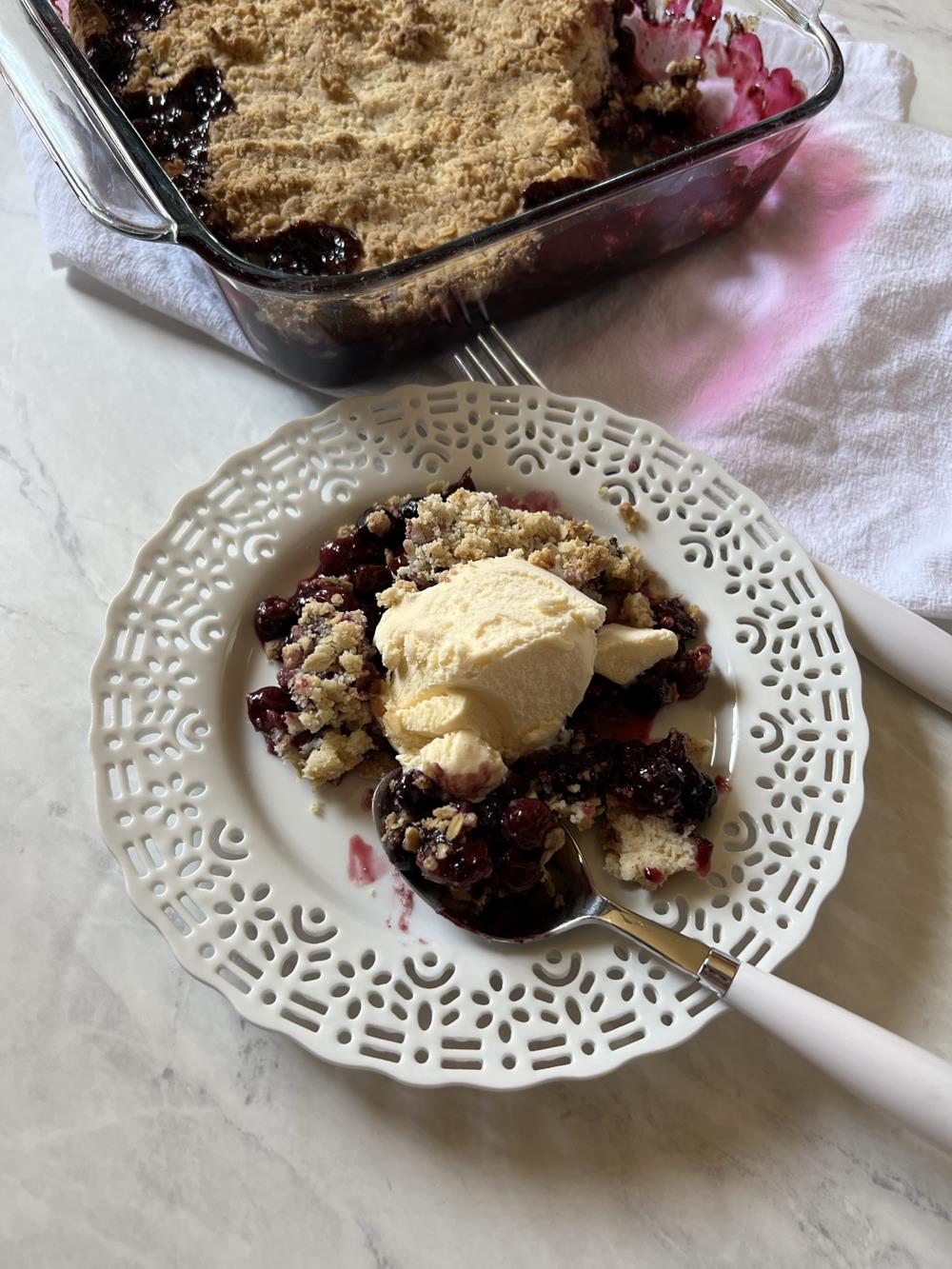 Blueberry crisp on white plate with glass pan in background