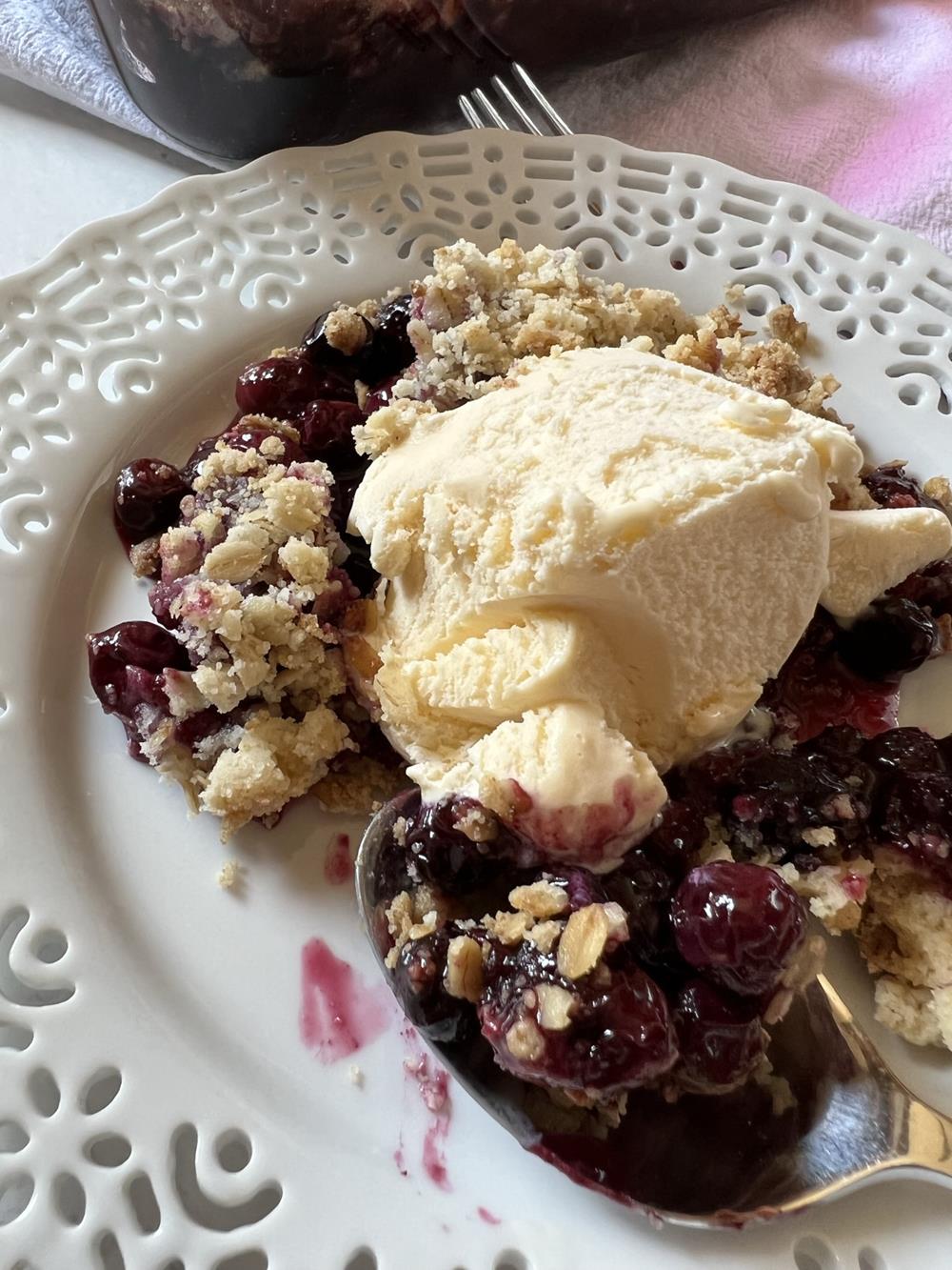 Blueberry crisp on white plate with spoon and ice cream