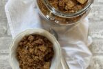 Peanut Butter Chex Granola in white bowl with spoon and glass jar background