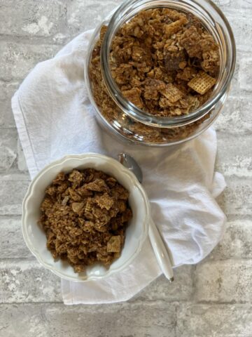 Peanut Butter Chex Granola in white bowl with spoon and glass jar background