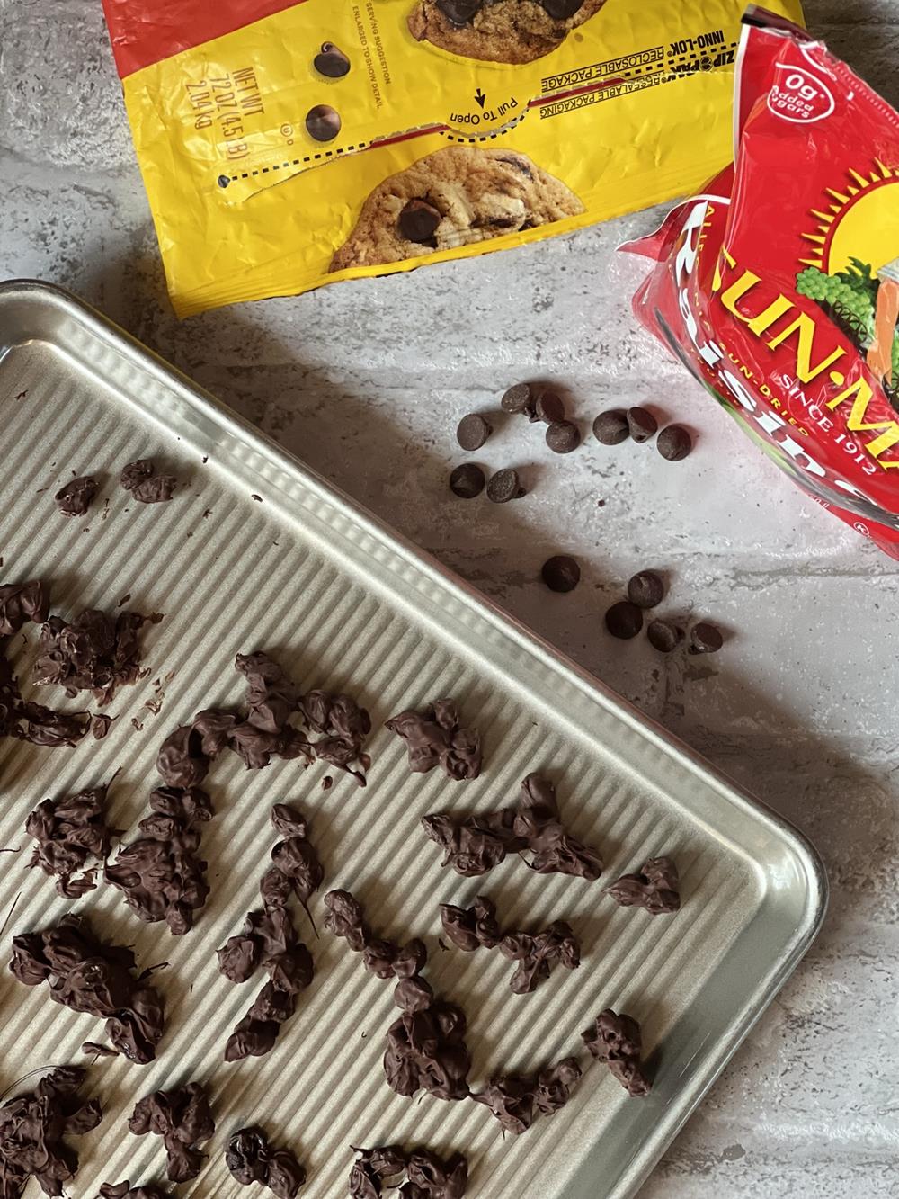 chocolate covered raisins on a cookie sheet with chocolate chips and raisins in background