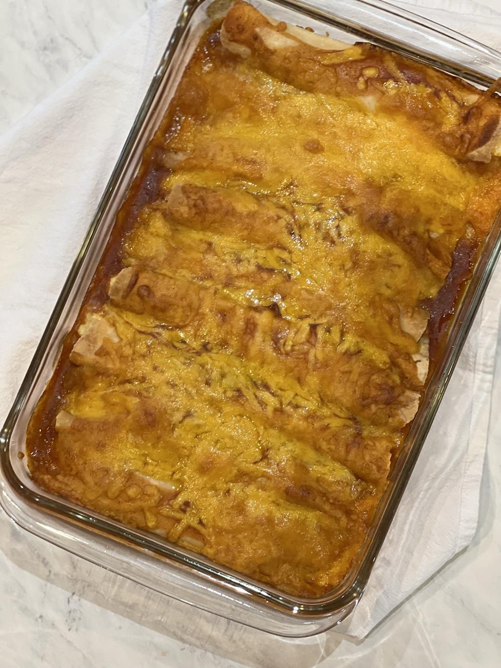 cooked enchiladas with red sauce and cheese in glass pan