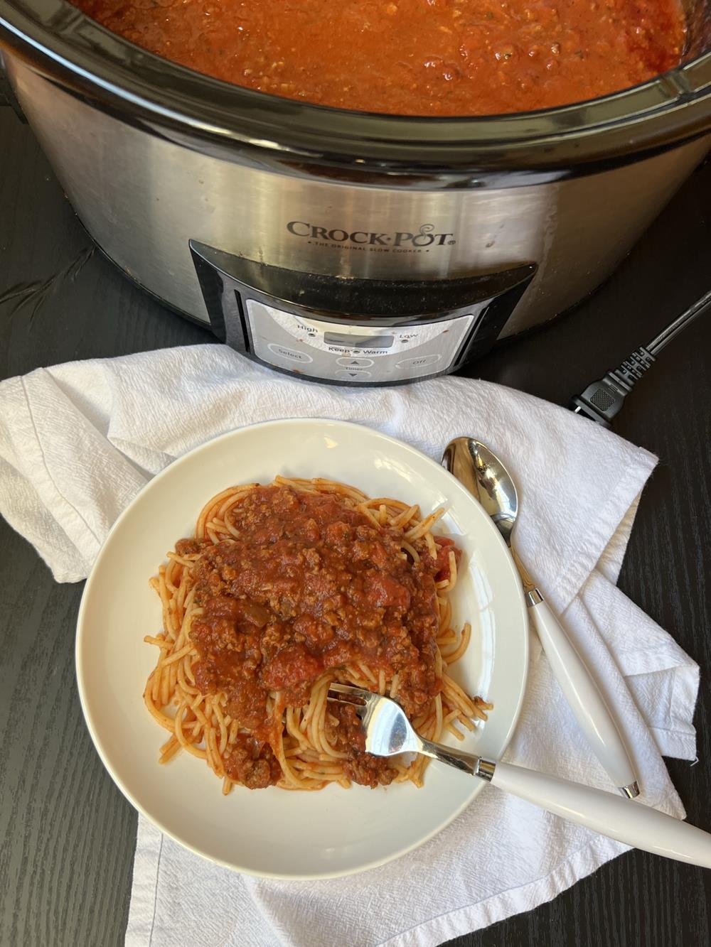 Crock Pot Spaghetti Sauce and pasta on white plate with crock pot in background