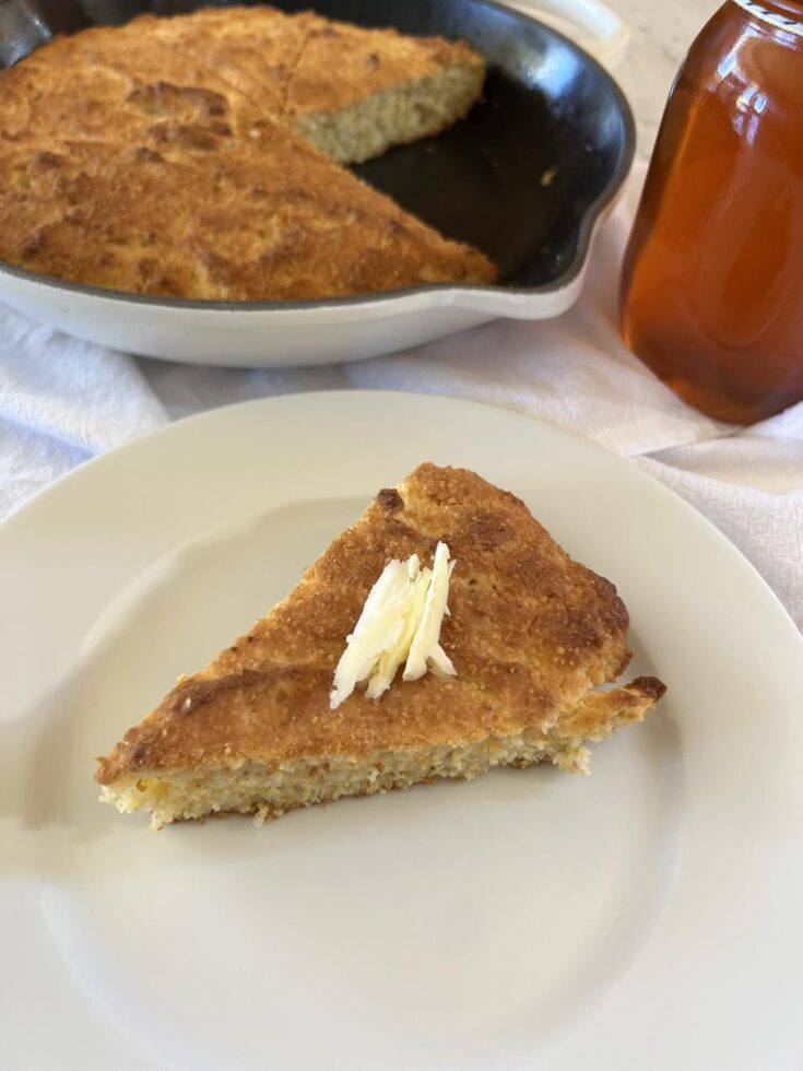 conbread on a plate with butter and a jar of honey in the background