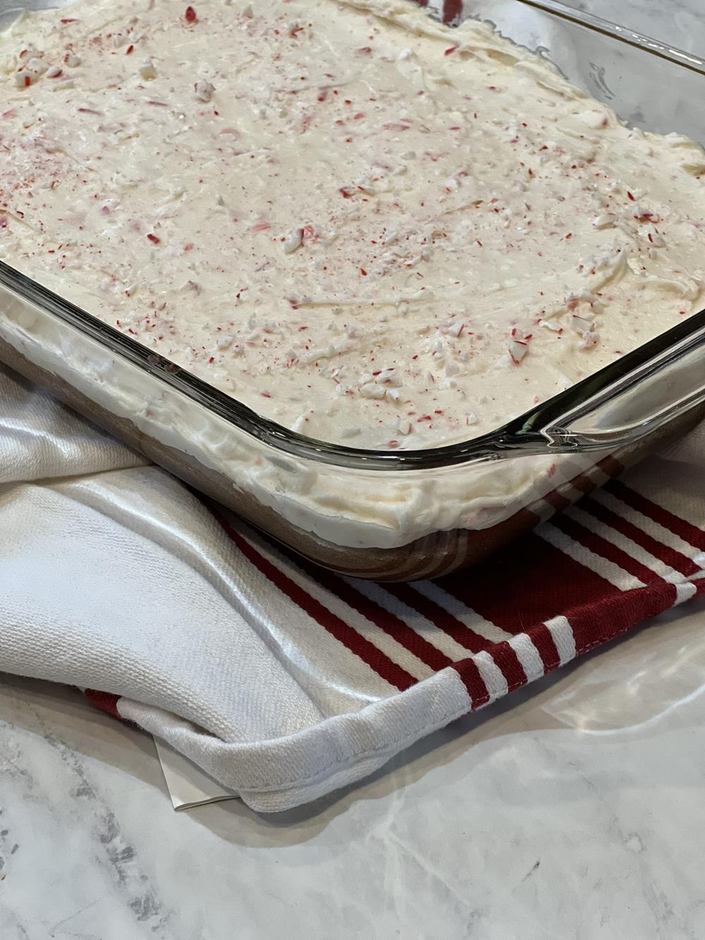 gluten free brownies with frosting in a glass pan with towel in background