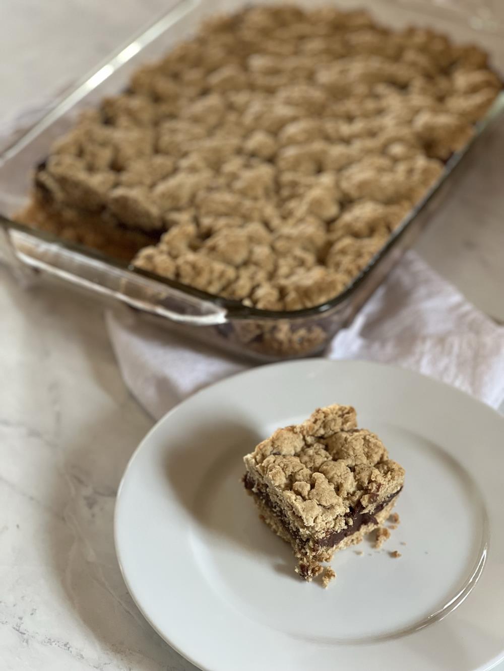 Gluten Free Fudge Bar on white plate with pan full of bars in background