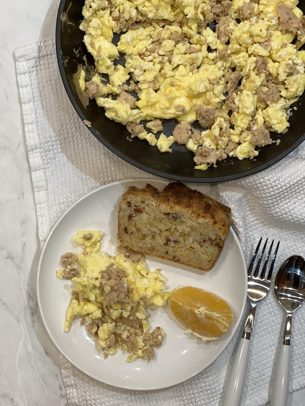 scrambled eggg on a white plate with bread and an orange