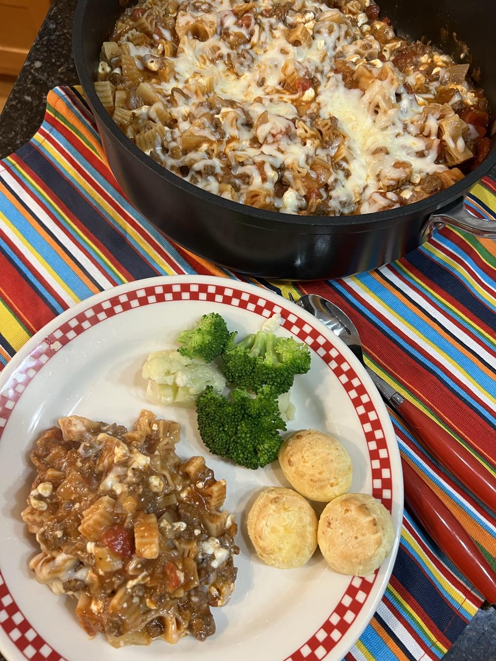 skillet lasagna on a red and white plate with broccoli and rolls