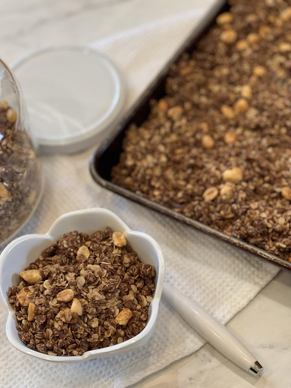 peanut butter granola in a white bowl with a jar and pan in the background