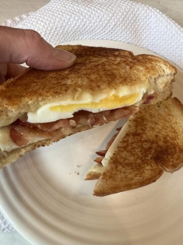 Bacon Egg and Cheese Grilled Cheese being picked up with white plate in background