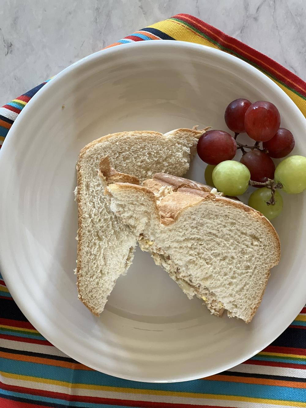 Salmon Salad Sandwich on white plate with read and green grapes