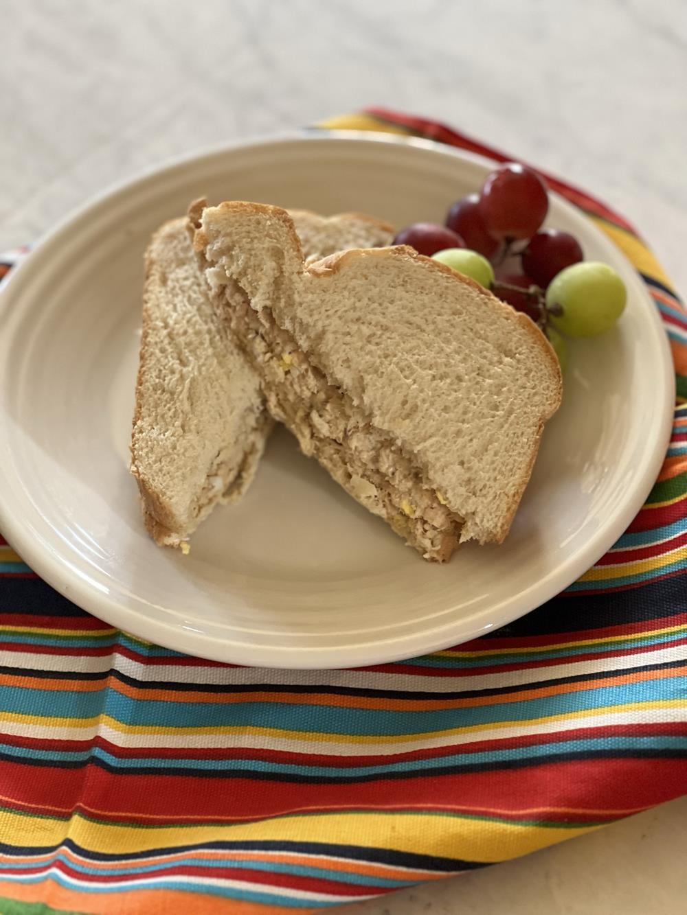 salmon salad sandwich on white plate with striped napkin