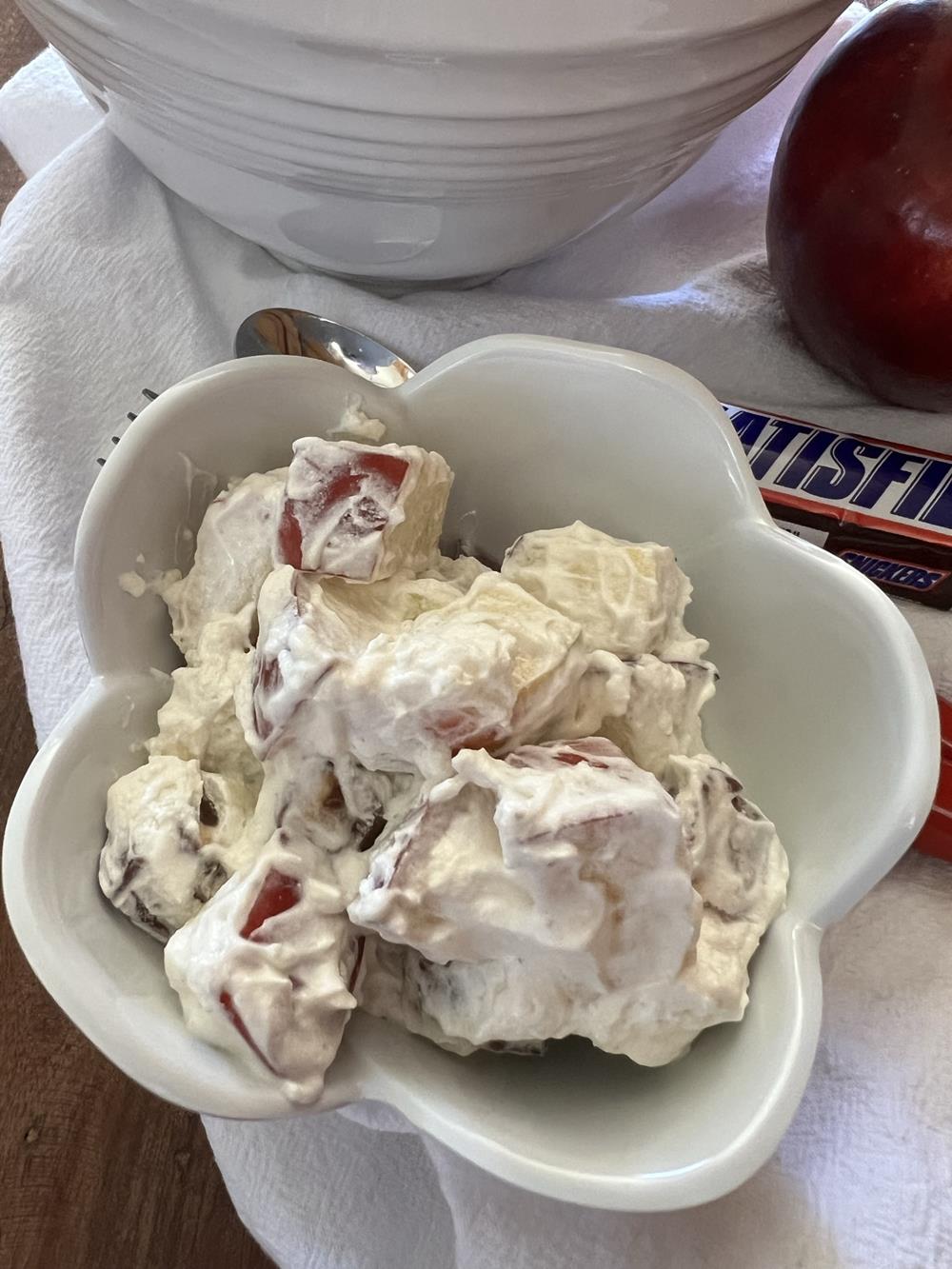 Snickers Apple Salad in white bowl with snickers bar and apple in background