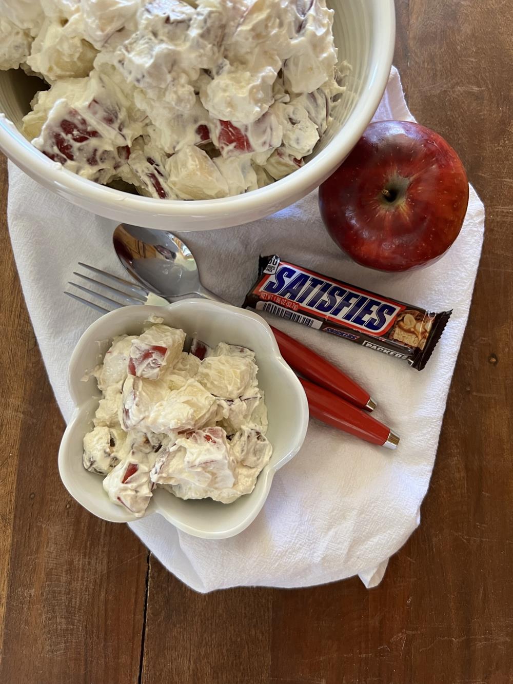 Snickers Apple Salad in white bowl with snickers bar and apple in background