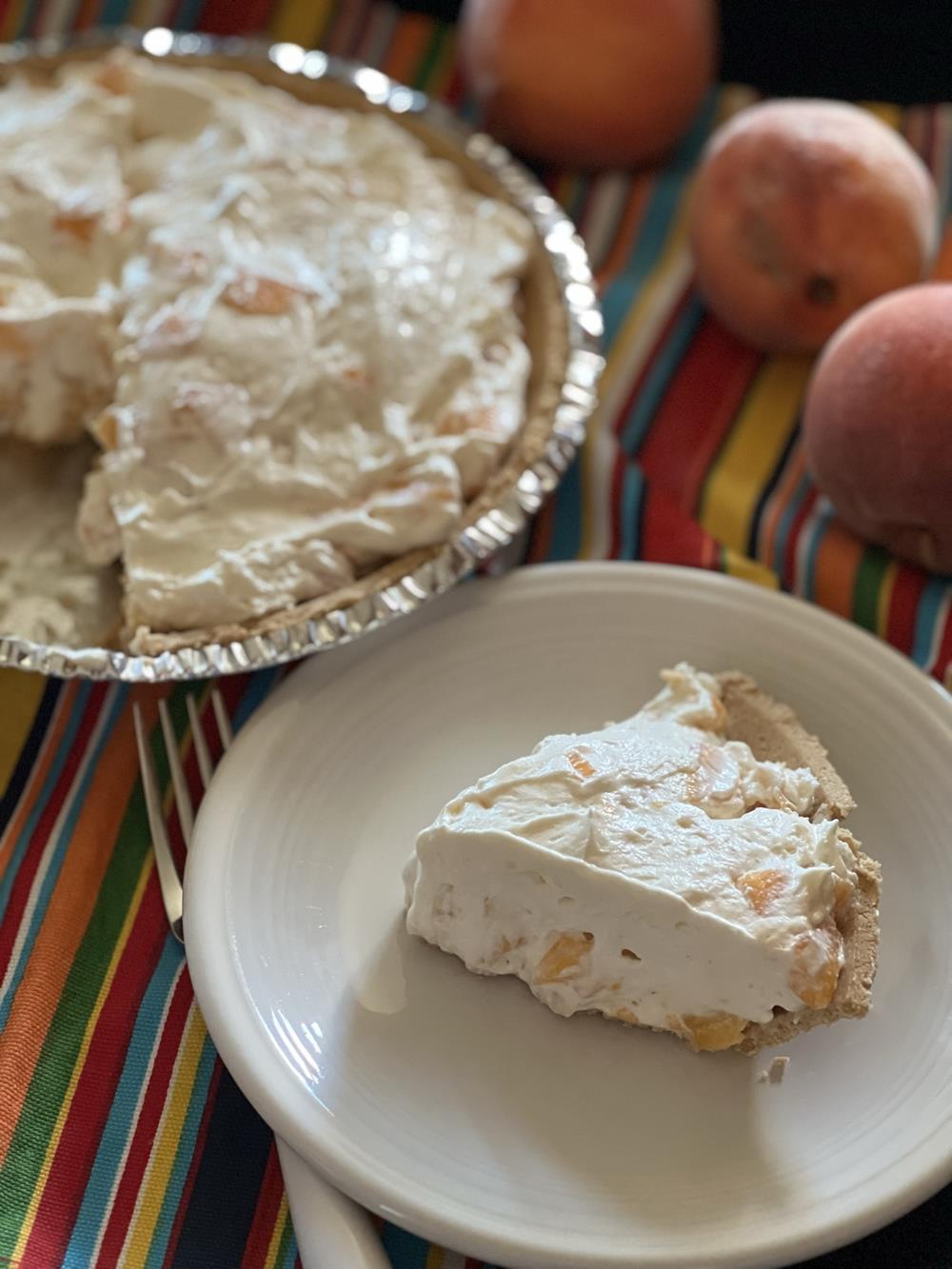 piece of peach pie on plate and peach pie on striped napkin with peaches next to it