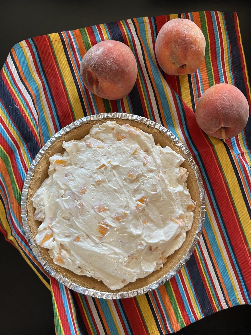 peach pie on striped napkin with peaches next to it