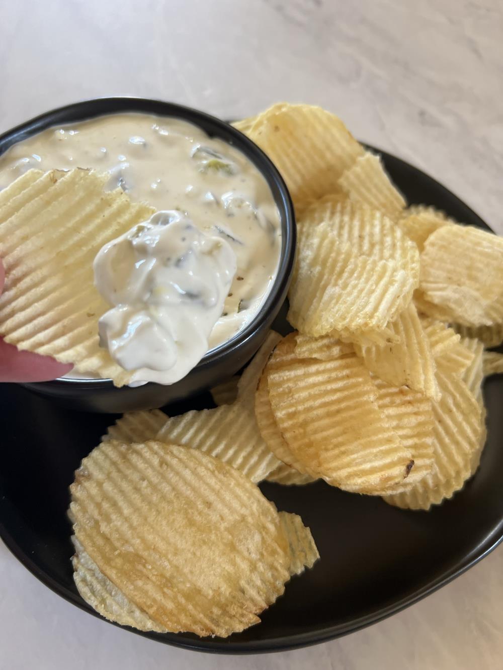 cream cheese pickle dip with potato chips on black dish on marble background