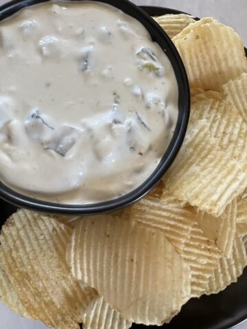 pickle dip with potato chips in black bowl on black plate