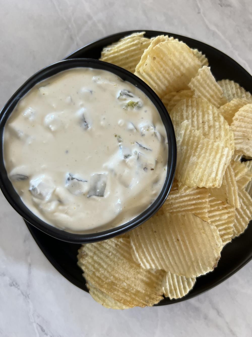 pickle dip in black bowl with potato chips on plate