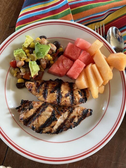 grilled chicken, fruit, and cowboy caviar on white and read plate.
