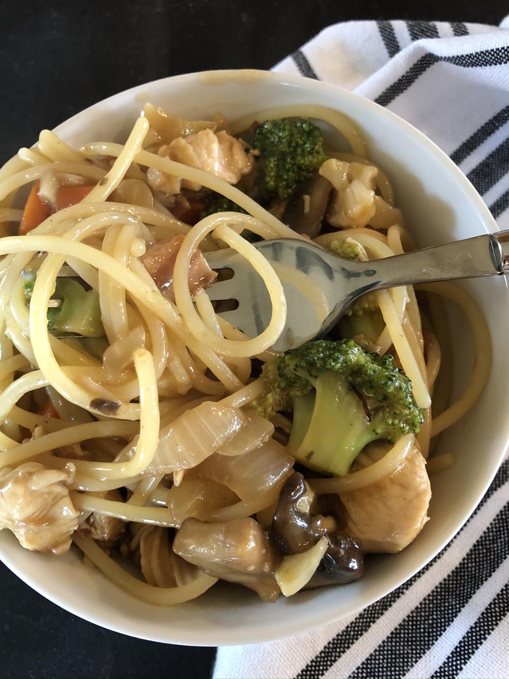 chicken bacon lo mein in white bowl with fork on black and white napkin