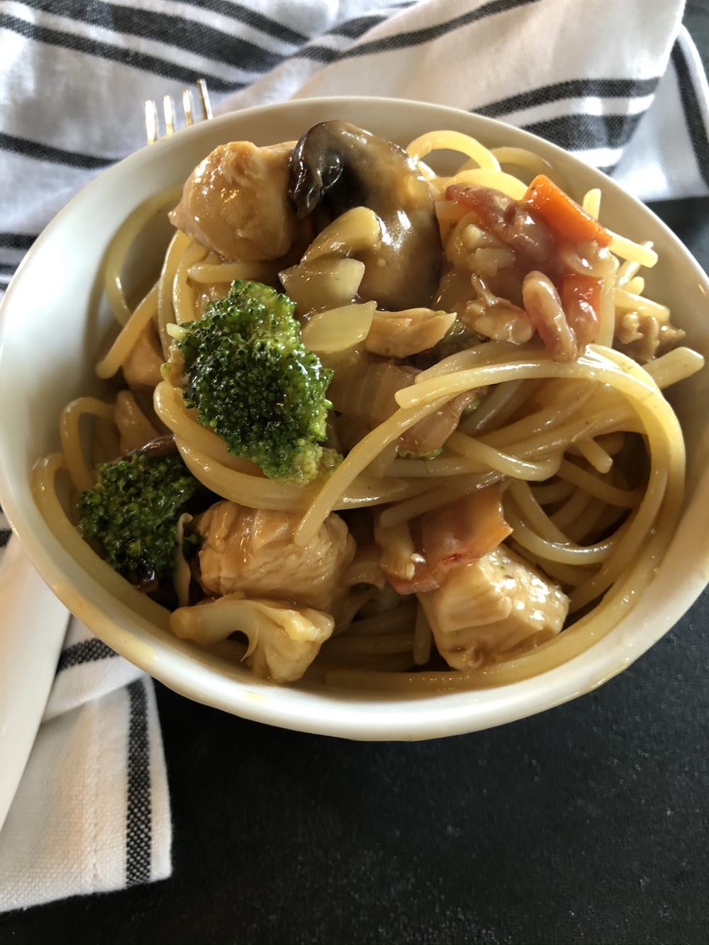 chicken low mein in white bowl with fork and black and white napkin