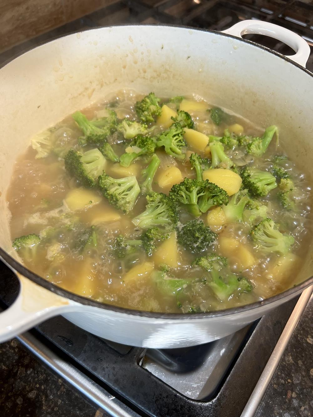 broccoli and potatoes cooking in broth in white pot