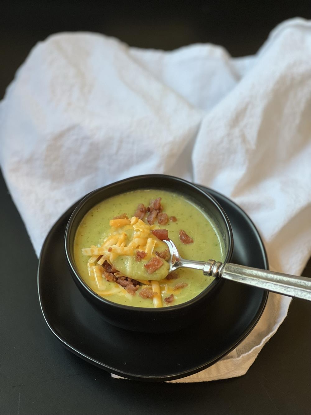 Martha Stewart's Broccoli Soup in a black bowl with spoon on white napkin