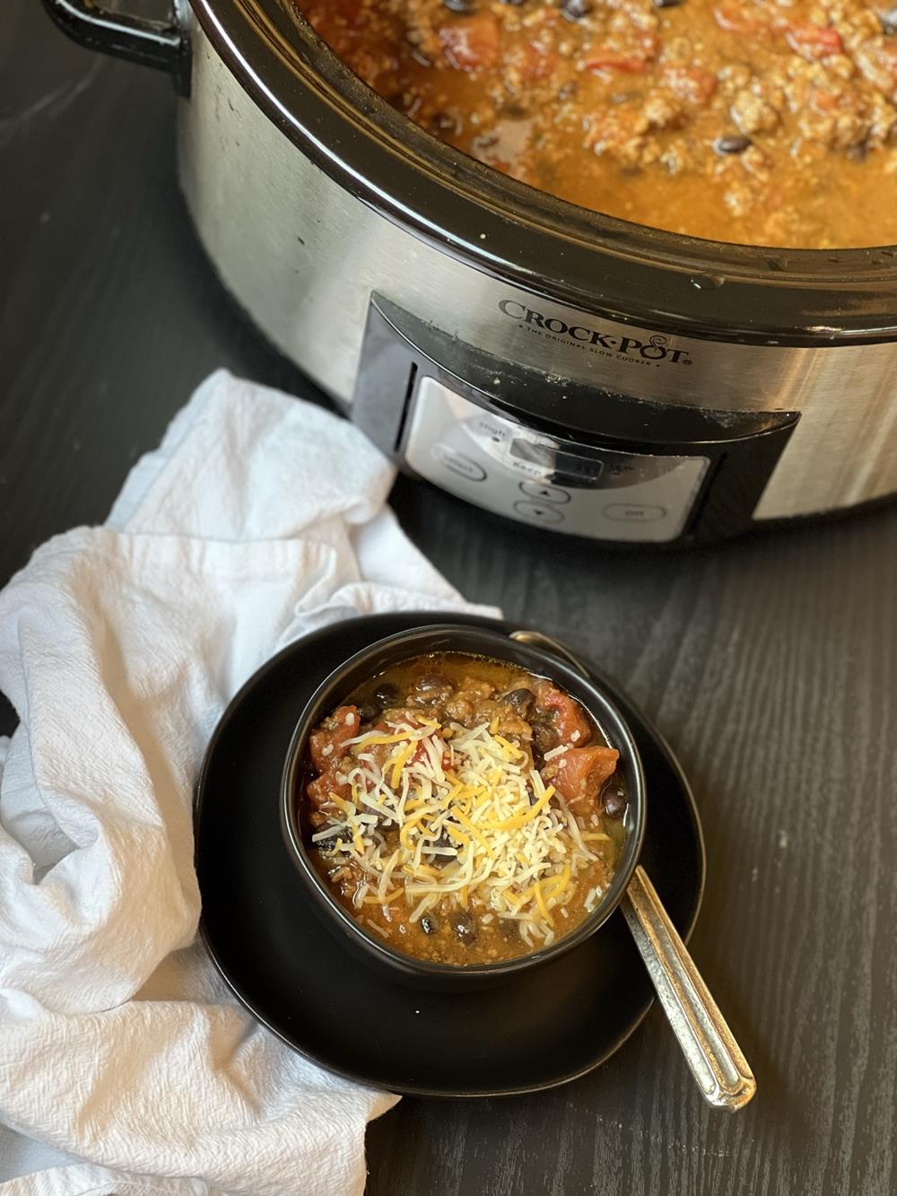 pumpkin chili in black bowl with crockpot full of chili in background