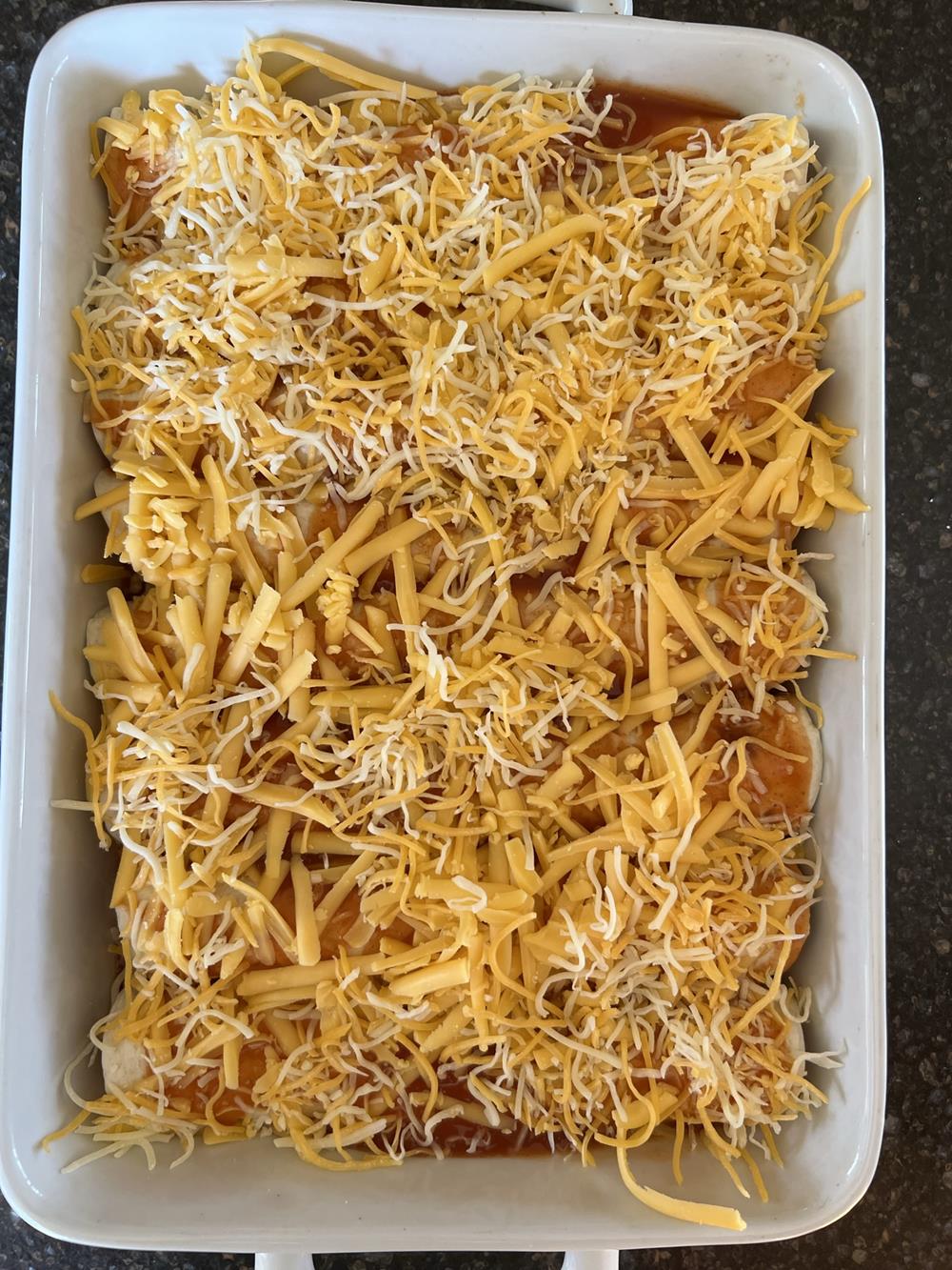 unbaked chicken enchiladas with cheese in white pan
