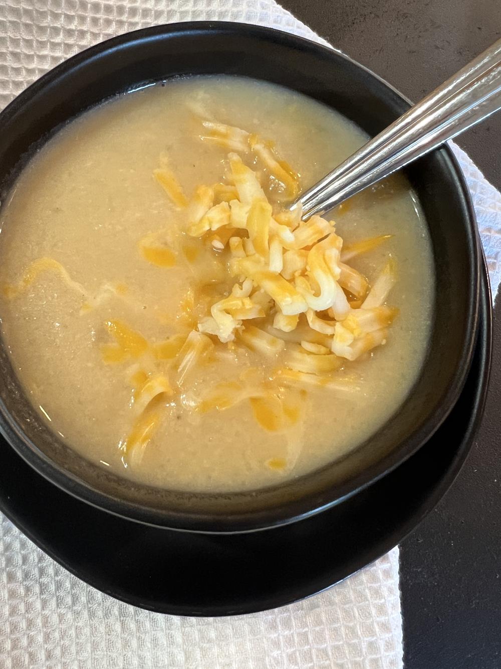 cauliflower soup in black bowl with spoon