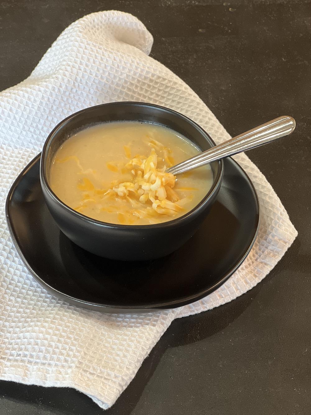 gluten free cauliflower soup with cheese in black bowl setting on white napkin