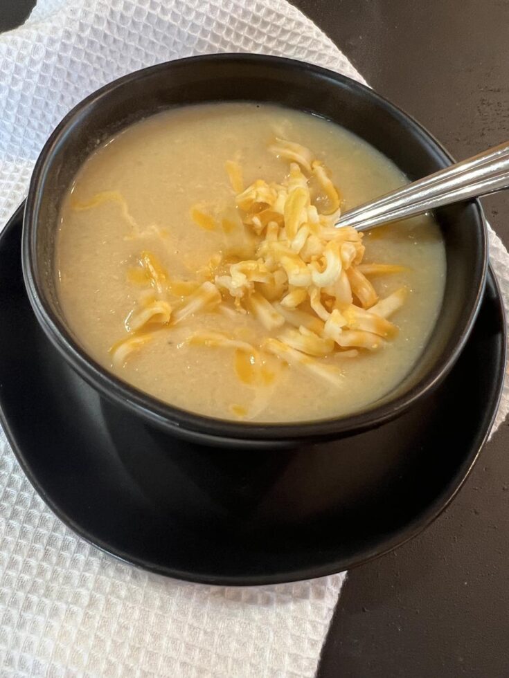 cauliflower soup with cheese in black bowl with spoon