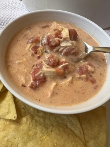 chicken queso soup in white bowl with spoon and chips on plate