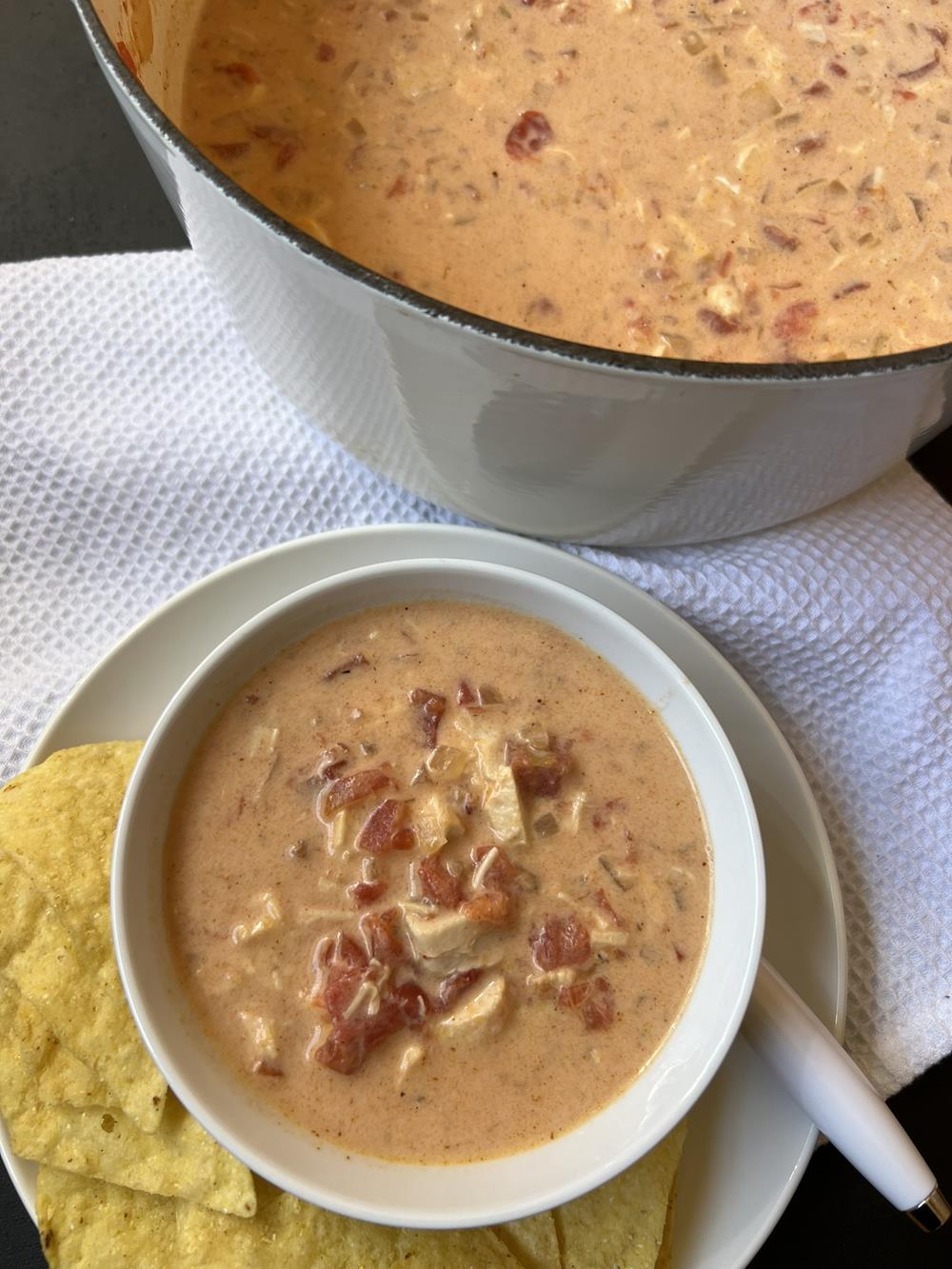 white bowl of chicken queso soup on white plate with chips in background