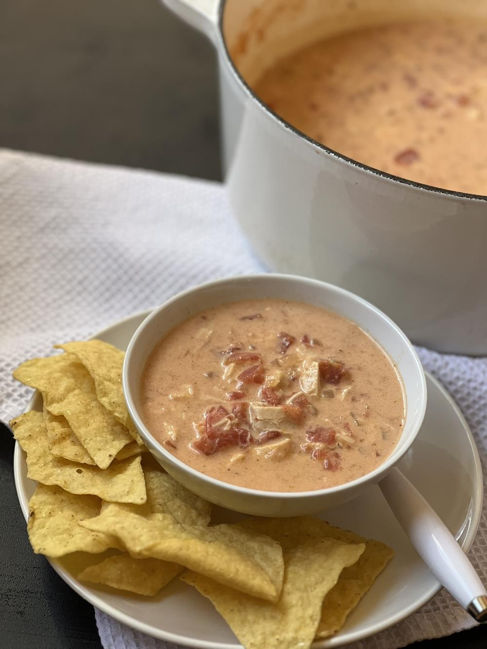 chicken cheese soup with tomatoes in white bowl on white plate with chips