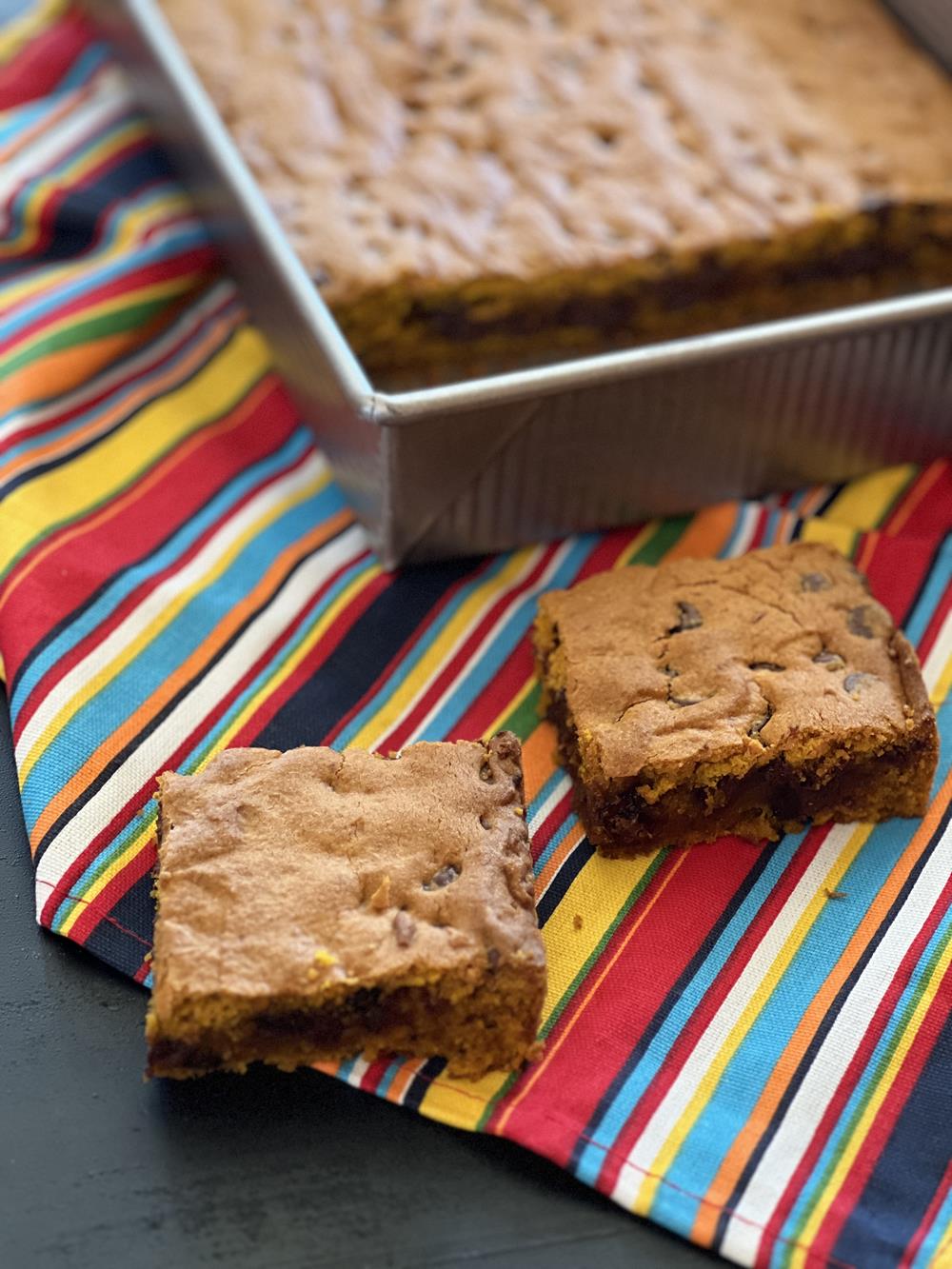 Gluten Free Pumpkin Chocolate Chip Bars on stiped napkin with pan of bars in background