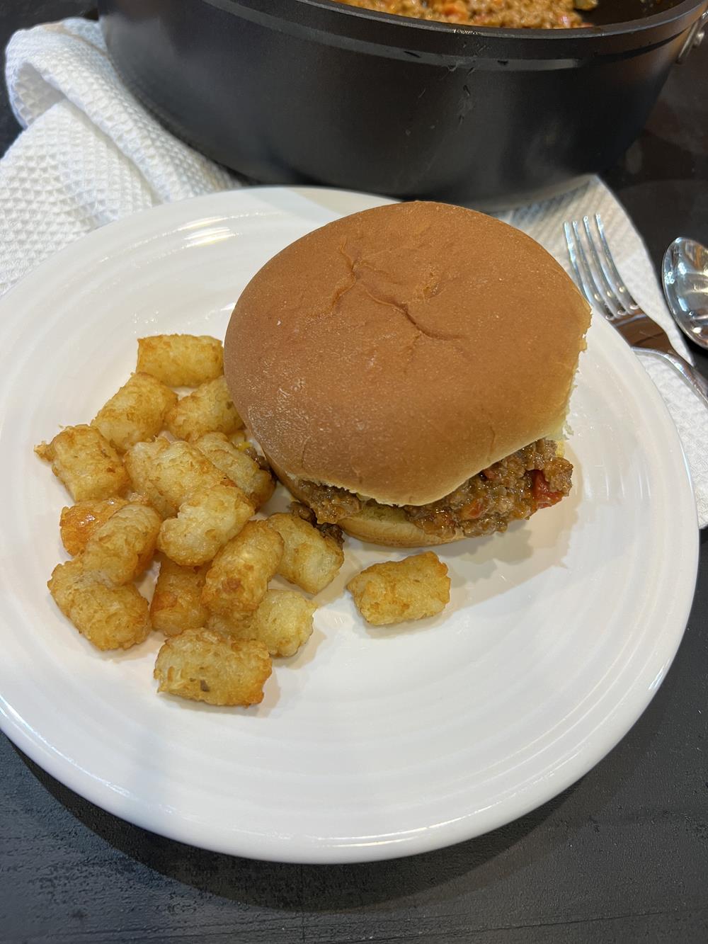 queso sloppy joes on bun with tater tots on white plate