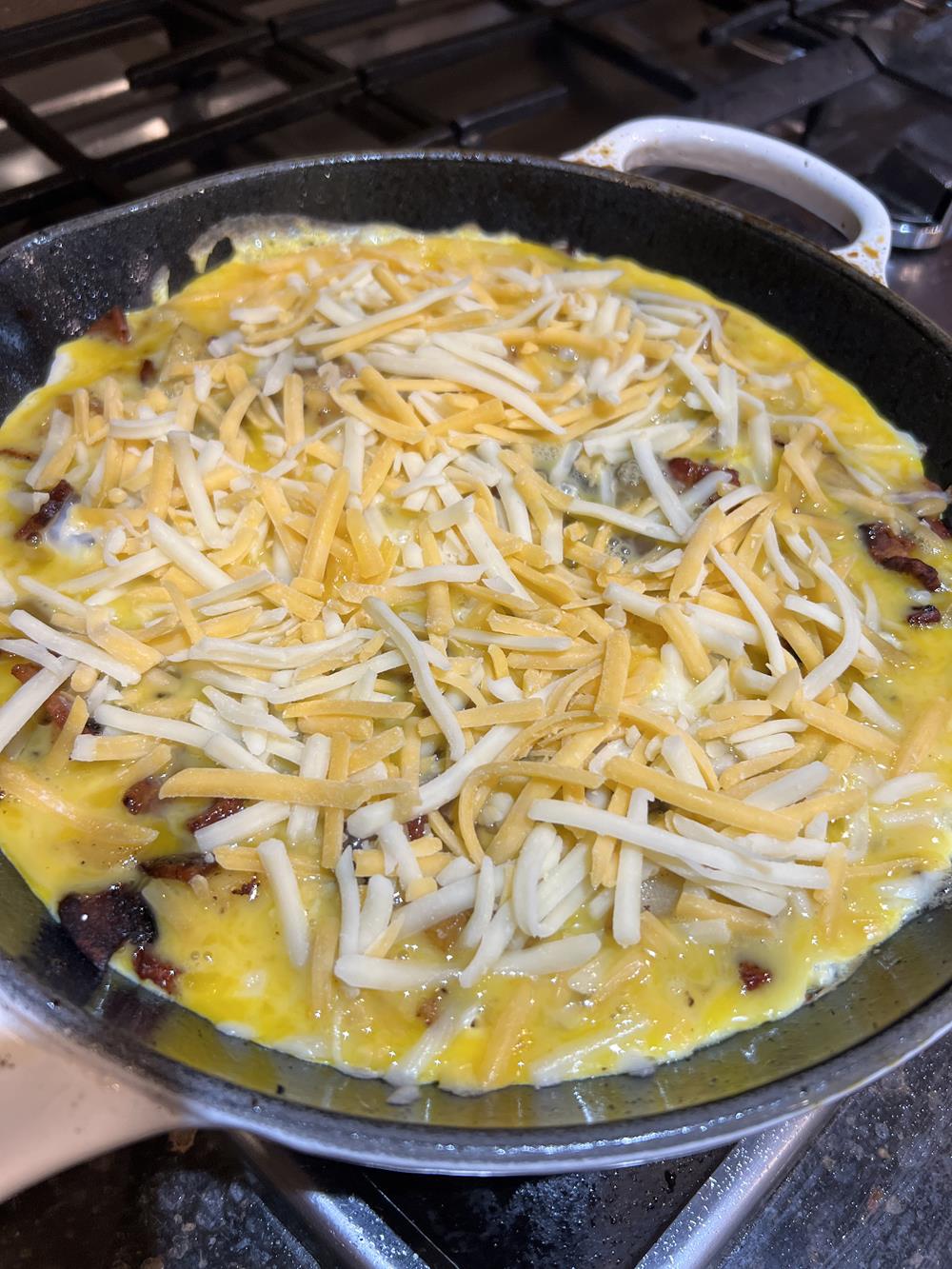 Apple Bacon Cheese Frittata Cooking in a cast iron pan on a stove